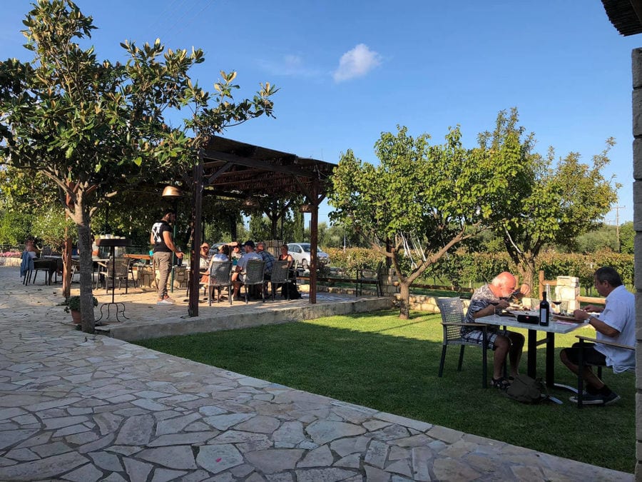 tourists sitting at the tables, drinking and eating surrounded by trees at Klima Grampsa outside